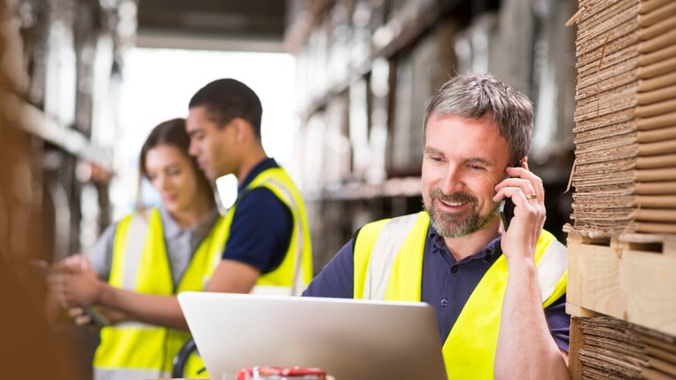 man in a warehouse using smartphone and laptop 