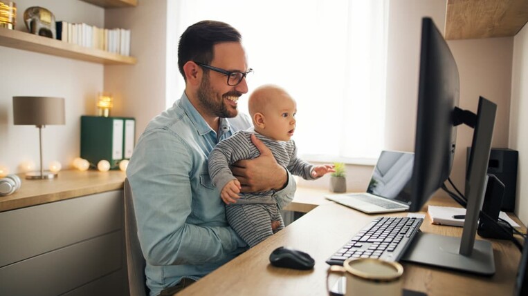 Vertriebler im Homeoffice hält sein Baby vor dem Bildschirm